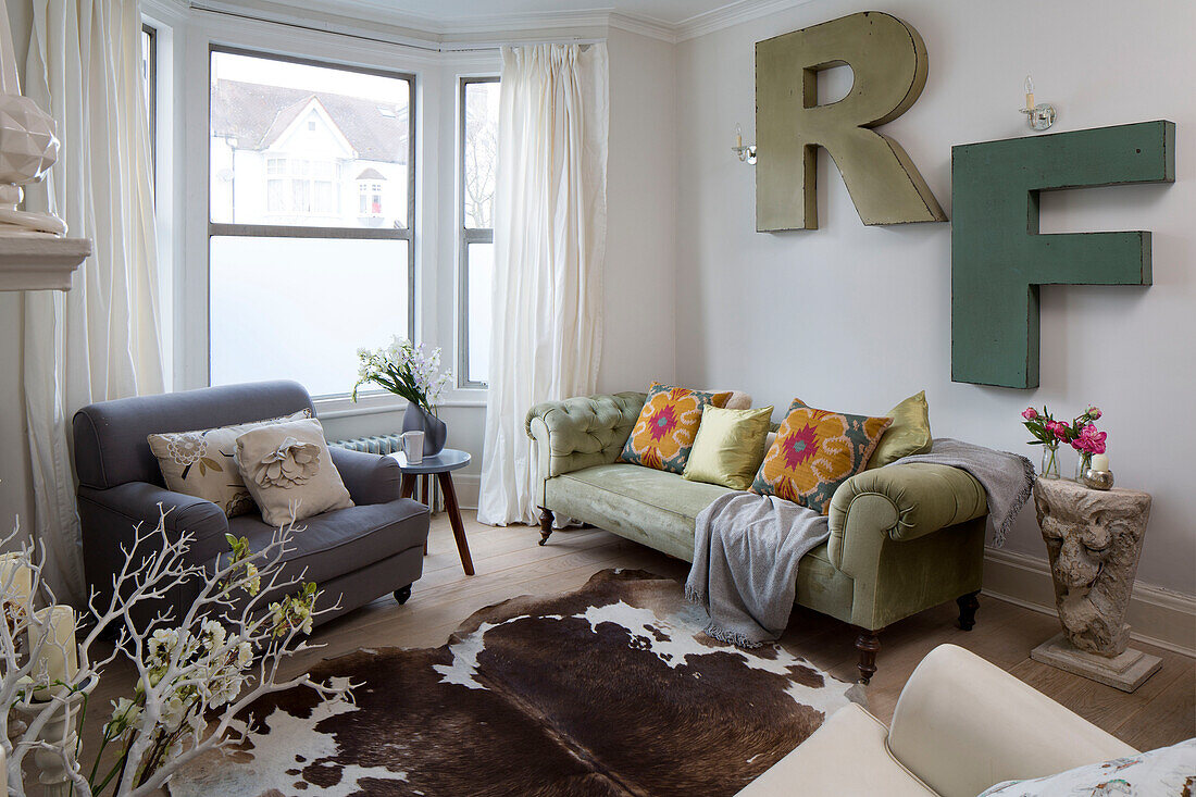 Geknöpftes Sofa und grauer Sessel mit an der Wand befestigten Buchstaben R und F im Wohnzimmer eines Londoner Stadthauses, England, UK