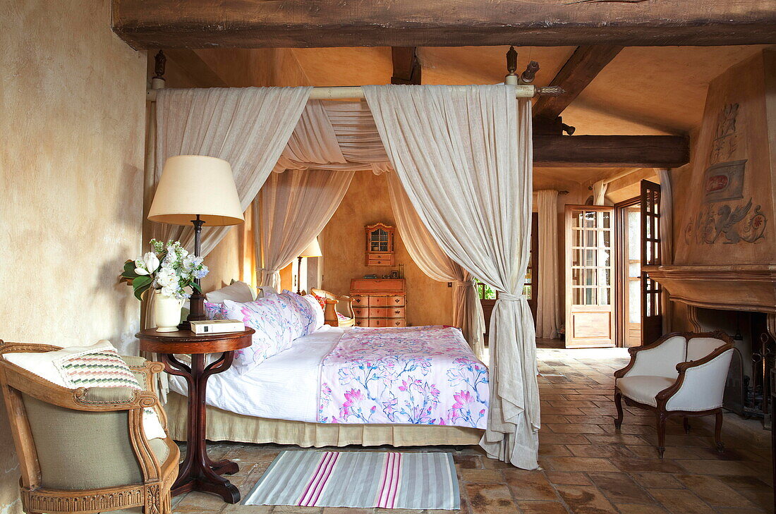 Himmelbett mit cremefarbenem Stoff in einem Schlafzimmer mit Steinfußboden in einer französischen Ferienvilla