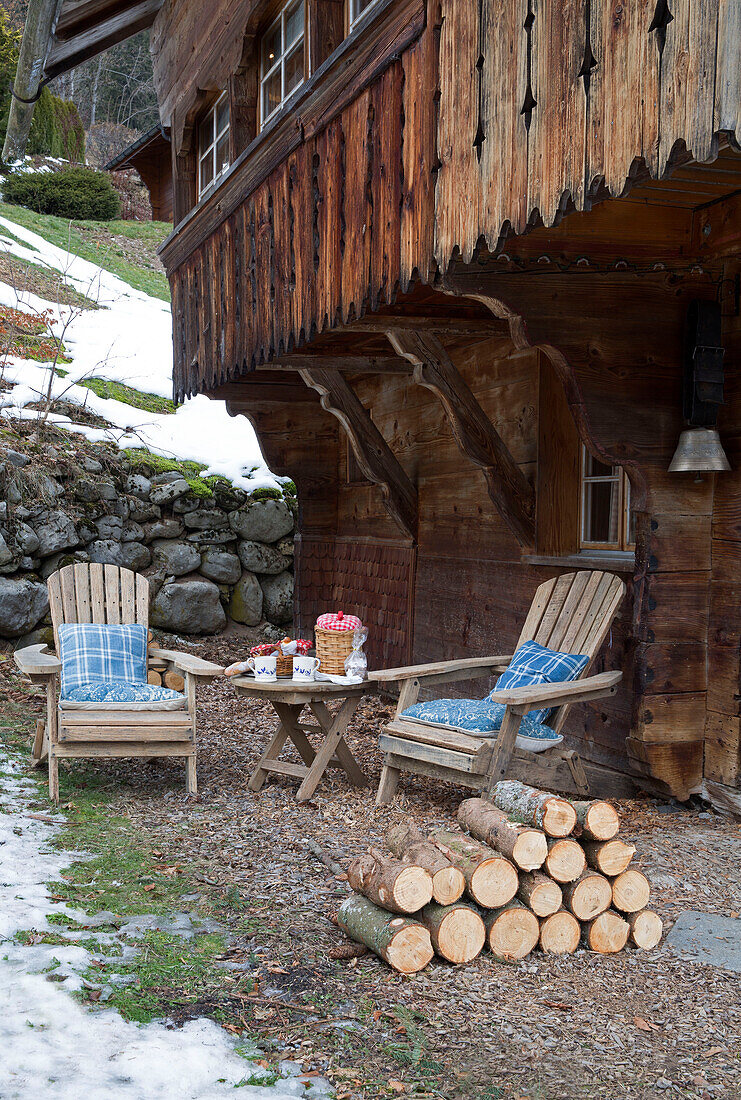 Pair of chairs with logs stacked, below carved balcony exterior of mountain chalet, Chateau-d'Oex, Vaud, Switzerland
