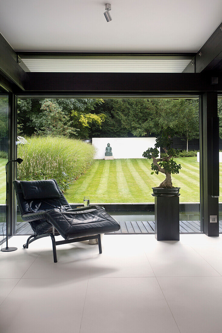 Schwarzer Ledersessel und Bonsai am Panoramafenster mit Blick auf den Garten in einem modernen Haus im Südwesten Londons England UK