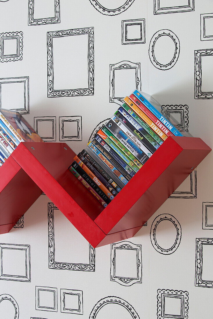 DVD-Sammlung auf rotem Regal mit Bilderrahmentapete in einem Londoner Familienhaus, England, UK
