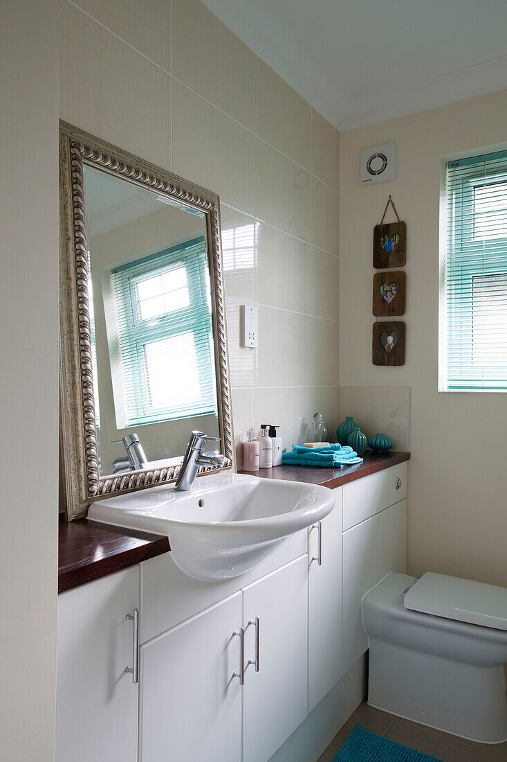 Cremefarben gefliestes Badezimmer mit weißem Einbauschrank und großem Spiegel in einem Einfamilienhaus in London, England, Vereinigtes Königreich