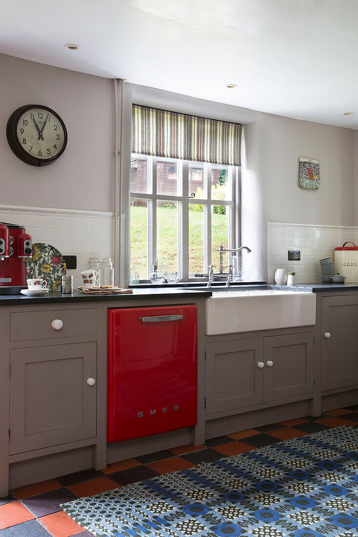 Rote Spülmaschine und Butler-Spüle unter einem Fenster mit Rollo in einer Küche in Ceredigion Wales UK