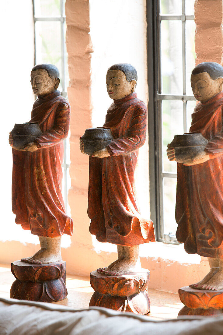 Statues of three Buddhist monks holding alms bowls on windowsill of London home, UK