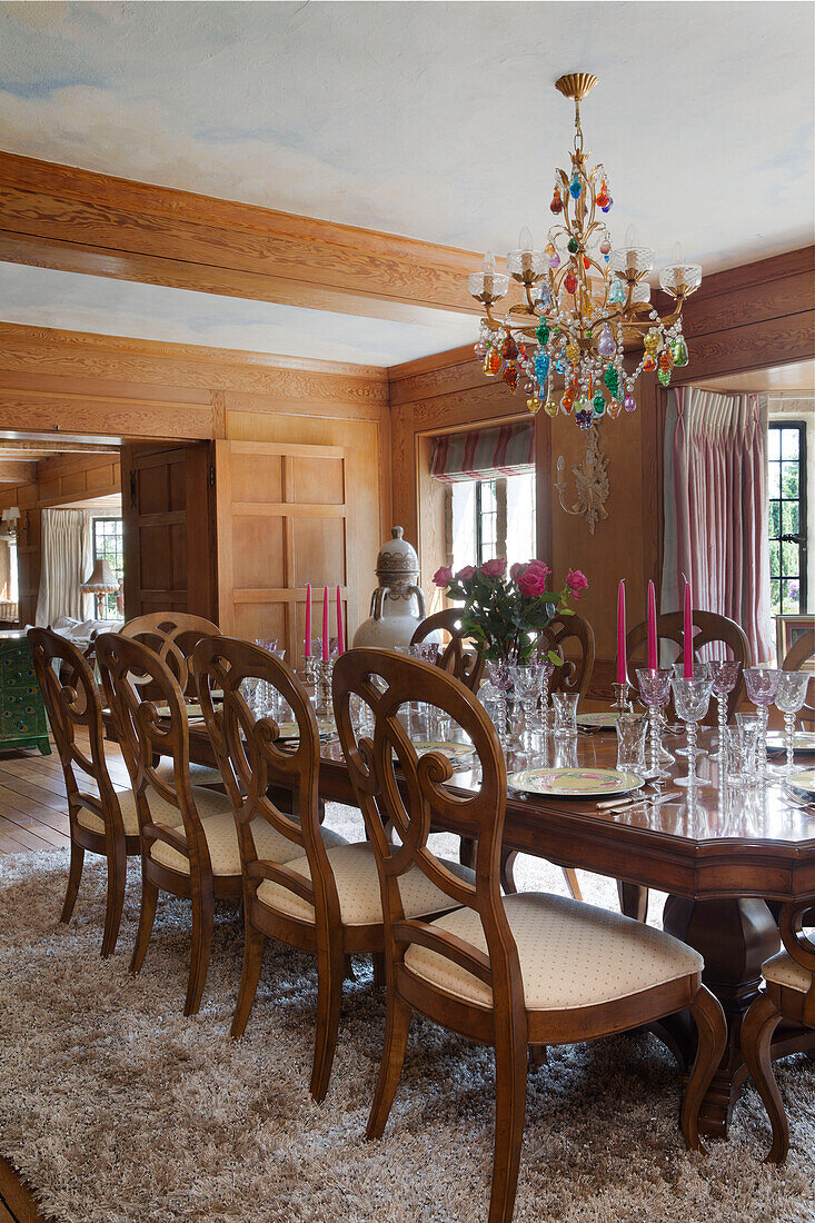 Glass chandelier above wooden dining table with glassware in London home, UK