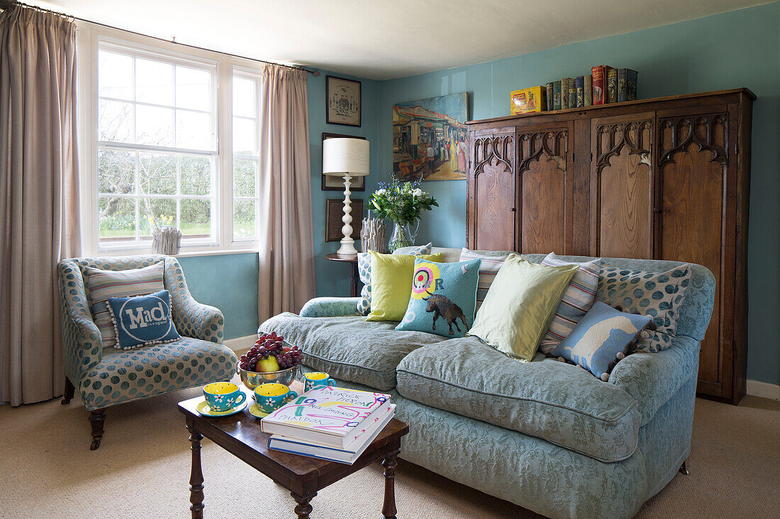 Assorted cushions on two seater sofa with wooden storage cupboard in Camber cottage East Sussex England UK