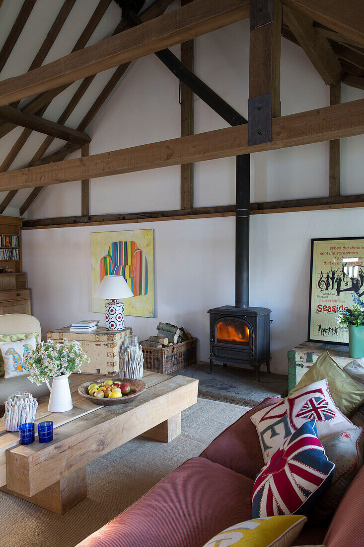 Cushions on pink sofa with low coffee table and lit woodburning stove in Camber cottage East Sussex England UK