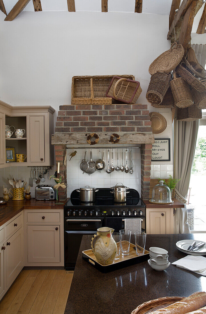 Exposed brick above black range oven with collection of baskets in modernised farmhouse kitchen, UK