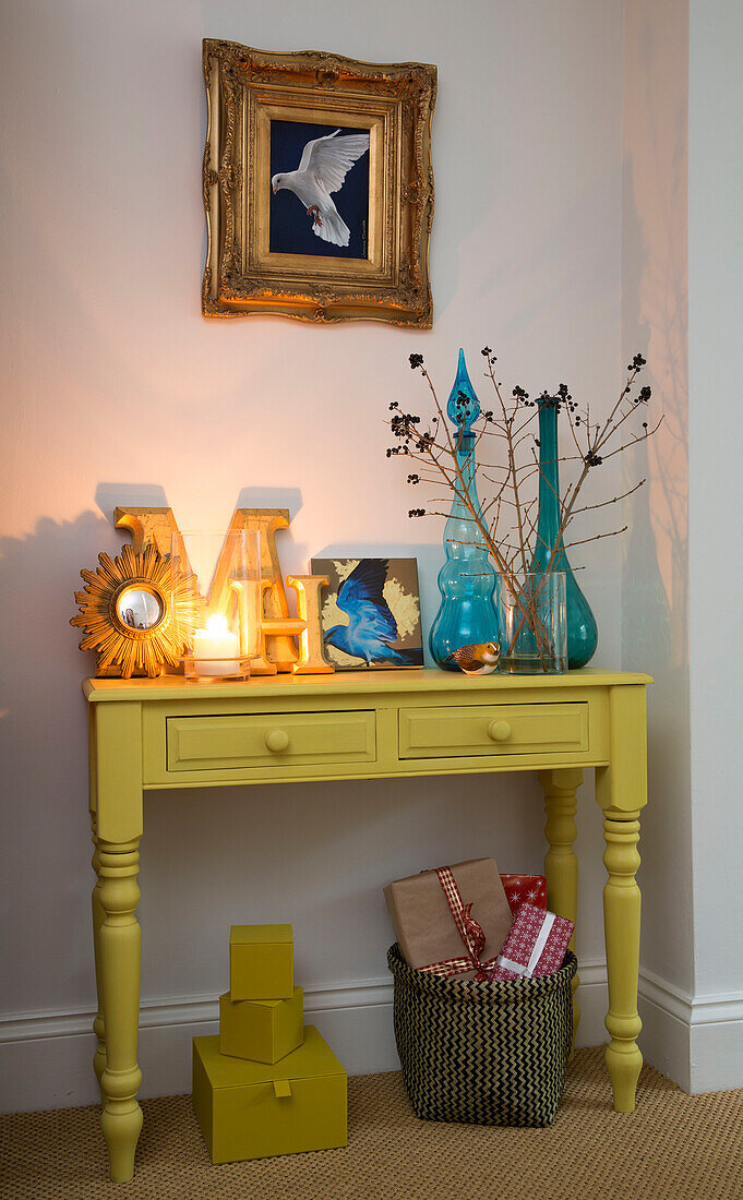 Bunte Glaswaren und eine brennende Kerze auf einem gelb gestrichenen Beistelltisch in einem Haus in London, England, UK