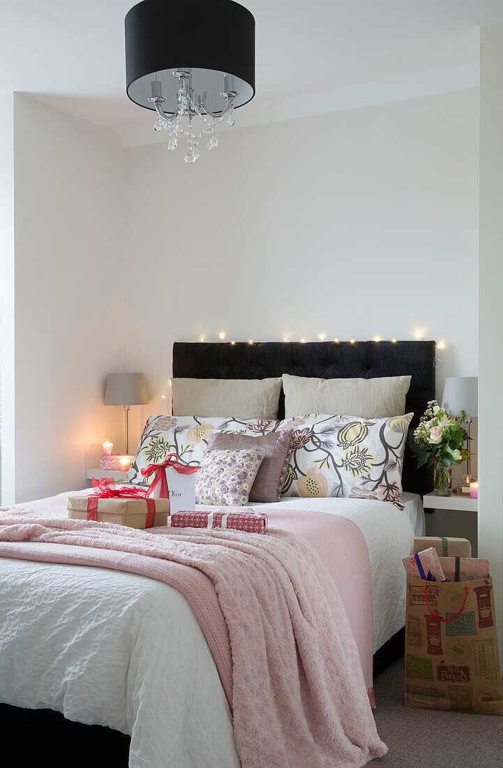 Black headboard and lampshade with pink blankets and gift wrapped presents on double bed in London home, England, UK
