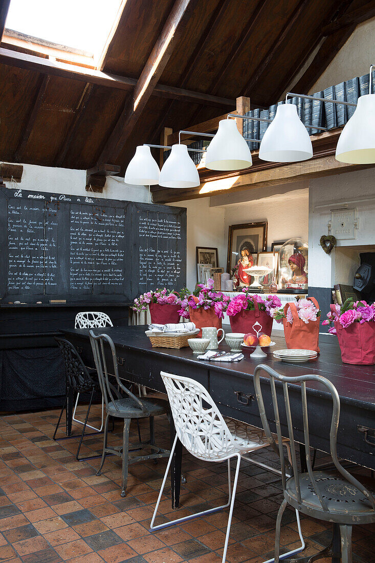 Pink centrepieces on dining table below pendant lights with menu on chalkboard in French farmhouse dining room