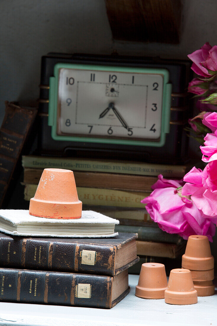 Rosa Rosen mit Uhr und Terrakotta-Blumentöpfen auf Nachschlagewerken in französischem Cottage