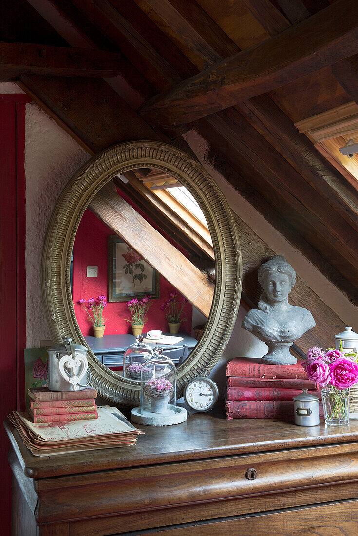 Ovaler Spiegel mit Büste und gebundenen Büchern auf Schlafzimmerkommode in einem französischen Bauernhaus-Schlafzimmer