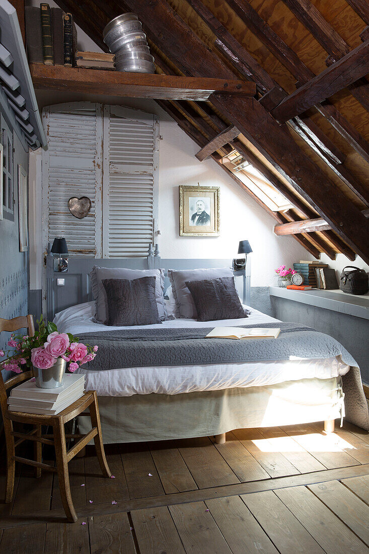Schnittblumen auf einem Holzstuhl am Fußende des Bettes in einem französischen Bauernhaus