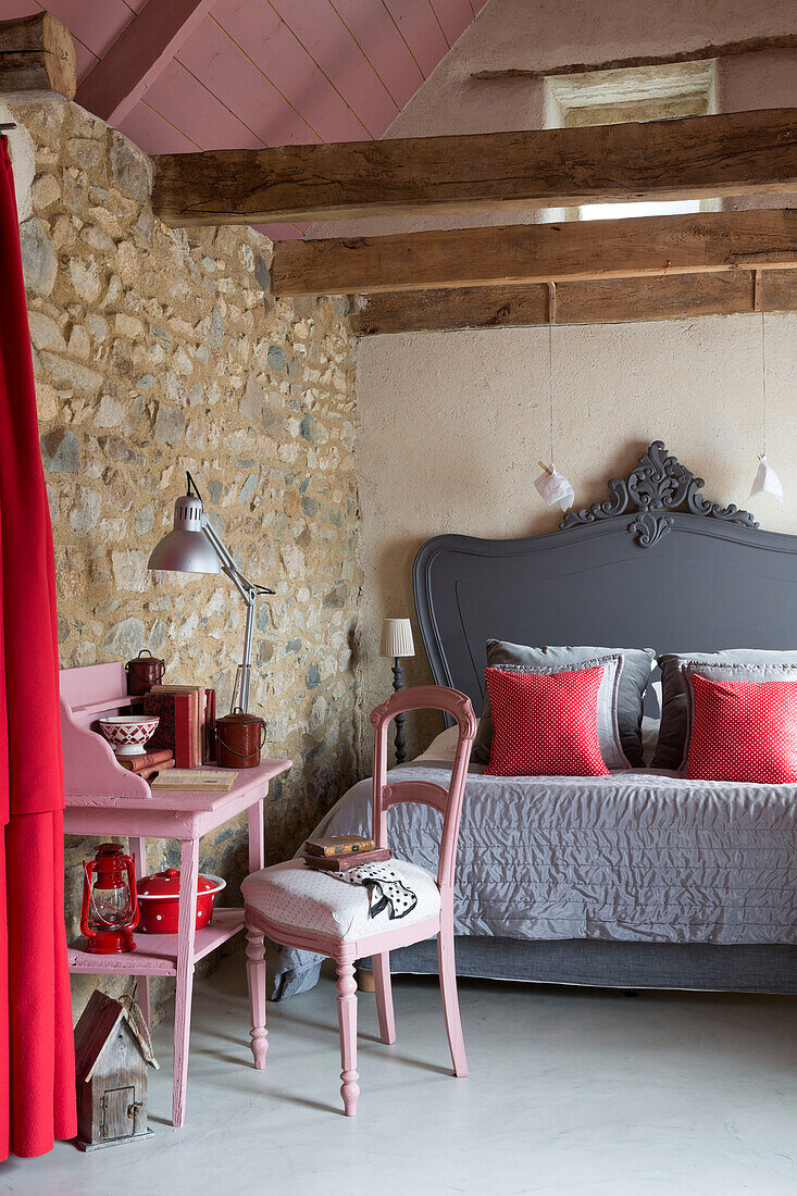 Rosa Schreibtisch und Stuhl mit grauem Doppelbett unter Deckenbalken in einem Schlafzimmer in einem bretonischen Landhaus, Frankreich