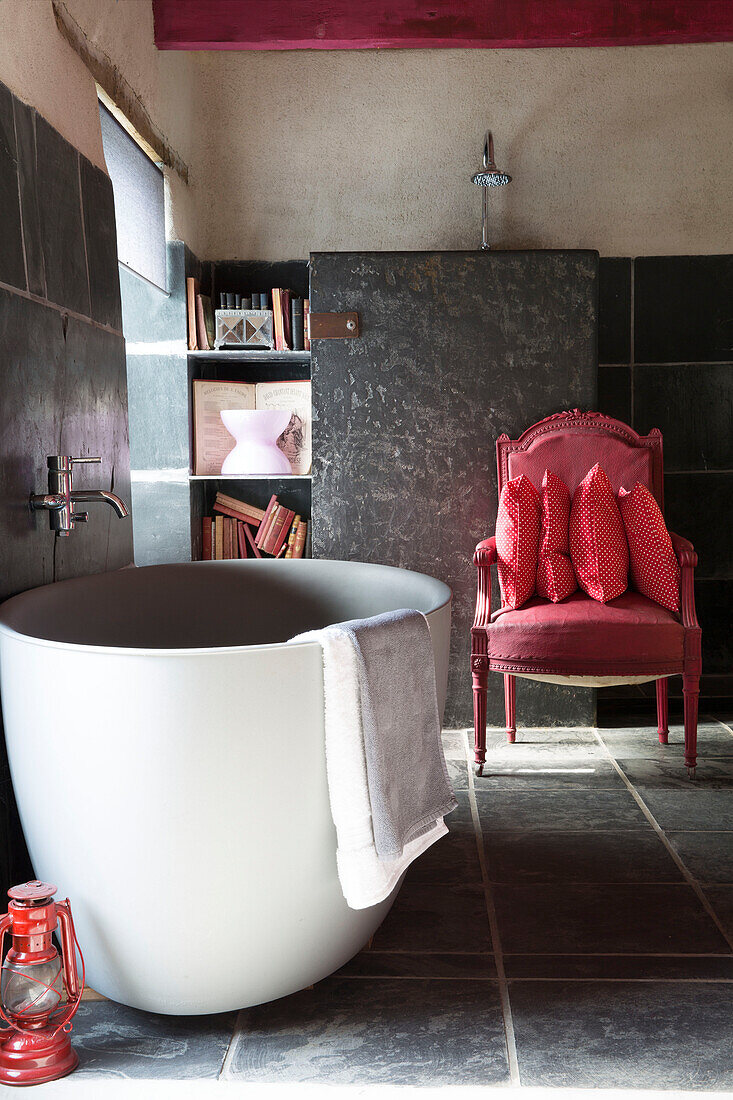 Freistehende Badewanne und roter Sessel in einem mit Schiefer gefliesten Badezimmer, bretonisches Landhaus, Frankreich