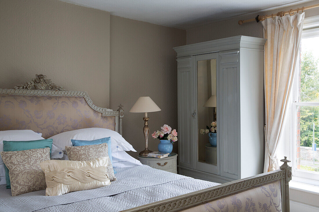 Gemalter Kleiderschrank und Doppelbett in einem Zimmer mit cremefarbenen Vorhängen und Raffhalter in einer britischen Wohnung