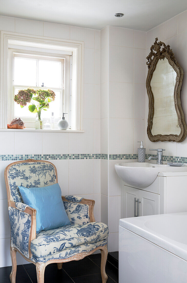 Hellblaues Kissen auf einem Toile de Jouy-Stuhl unter einem quadratischen Fenster im Badezimmer einer britischen Wohnung