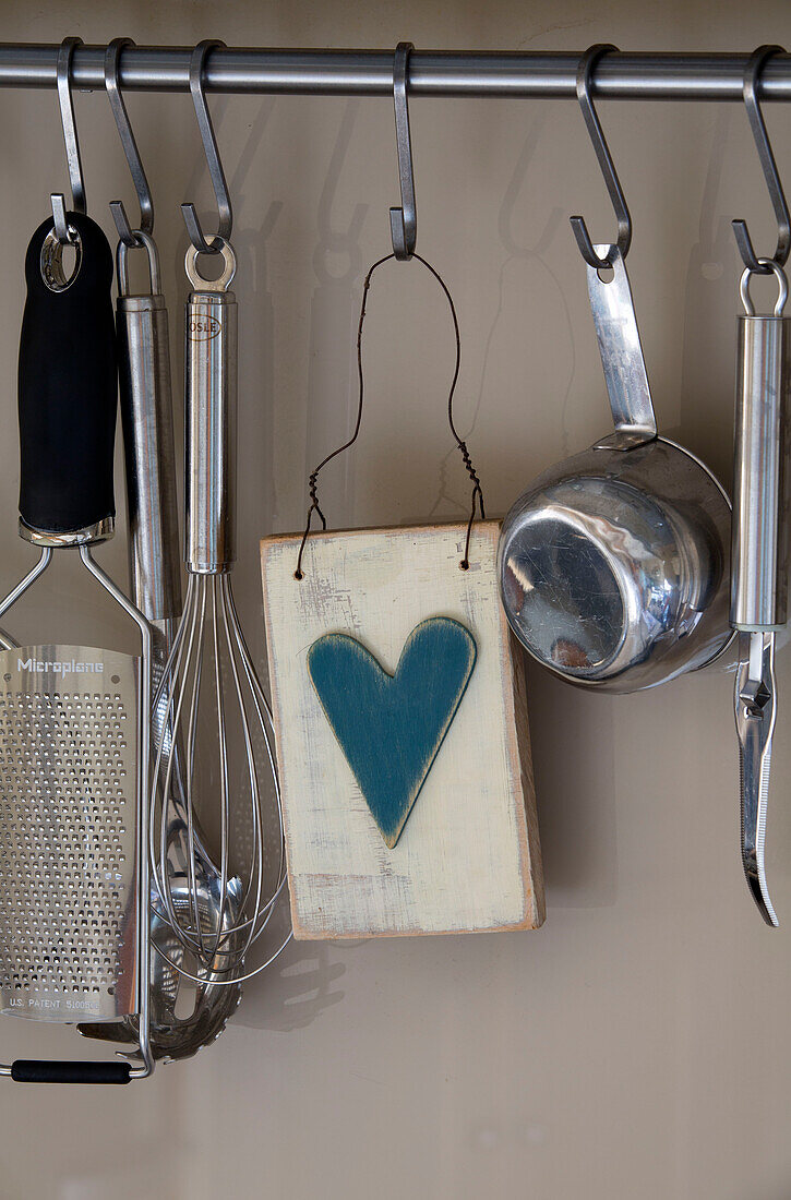 Küchenutensilien und Herz-Ornament hängen an der Geschirrstange in der Küche eines Suffolk-Bauernhauses, England, UK