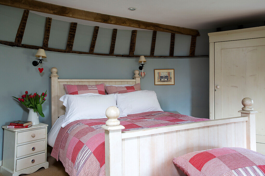 Patchwork-Quilt mit geschnittenen Tulpen am Bett in einem Bauernhaus mit Balken in Suffolk, England, UK