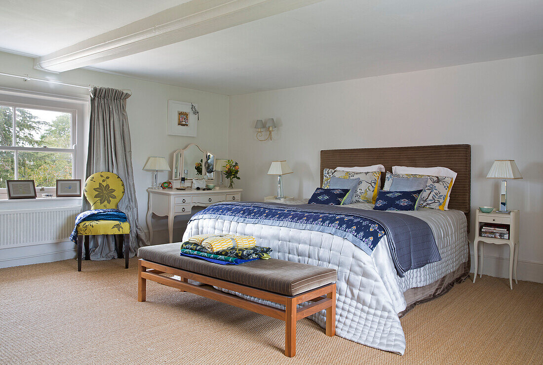 Blaue Steppdecken und Kissen auf einem Doppelbett mit Fußbank in einem Schlafzimmer mit Kokosfasermatten, London, England, UK