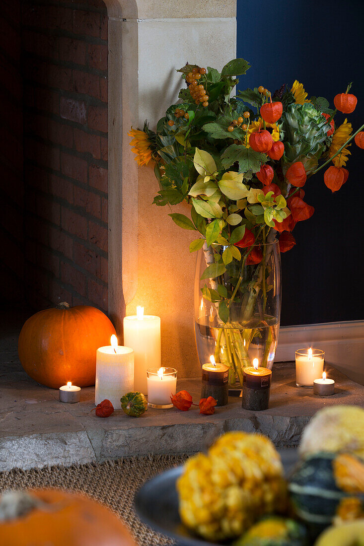 Schnittblumen und brennende Kerzen mit Kürbis am Kamin in einem Londoner Haus, England, UK