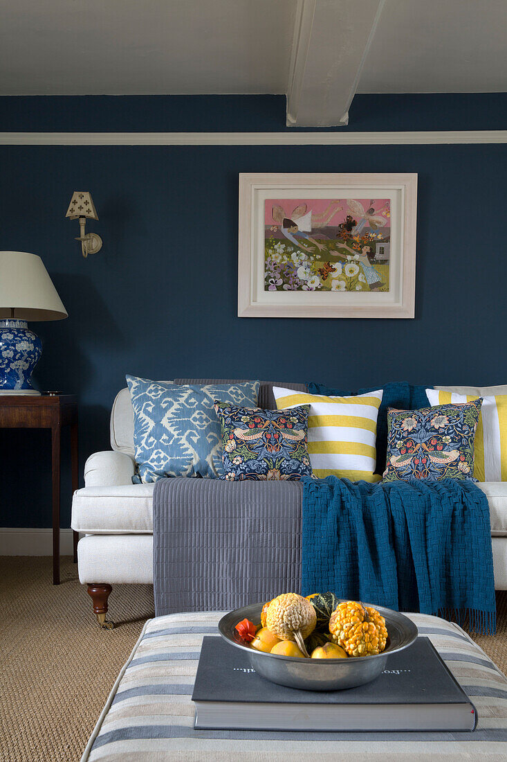 Framed artwork above sofa with assorted cushions and bowl of gourds in London home,  England,  UK