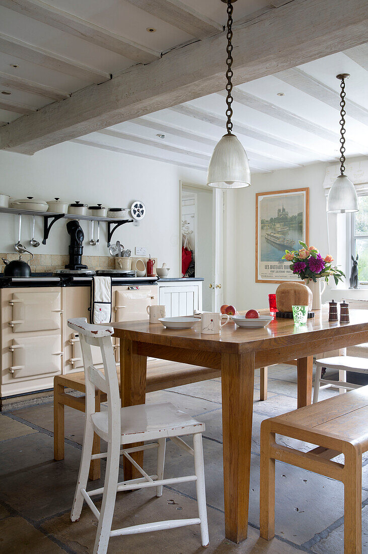 Glas-Pendelleuchten über Holztisch mit Bänken in einer mit Fliesen ausgelegten Küche in einem Londoner Haus, England, Vereinigtes Königreich
