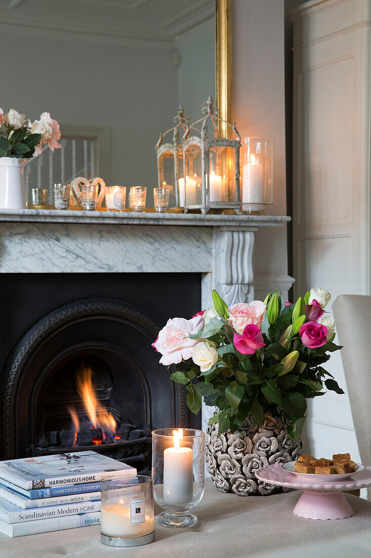 Cut flowers with lit candles and fire in living room of Hertfordshire home,  England,  UK
