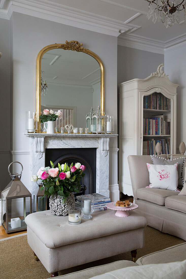 Gilt framed mirror on mantlepiece with cut flowers on ottoman in Hertfordshire living room,  England,  UK