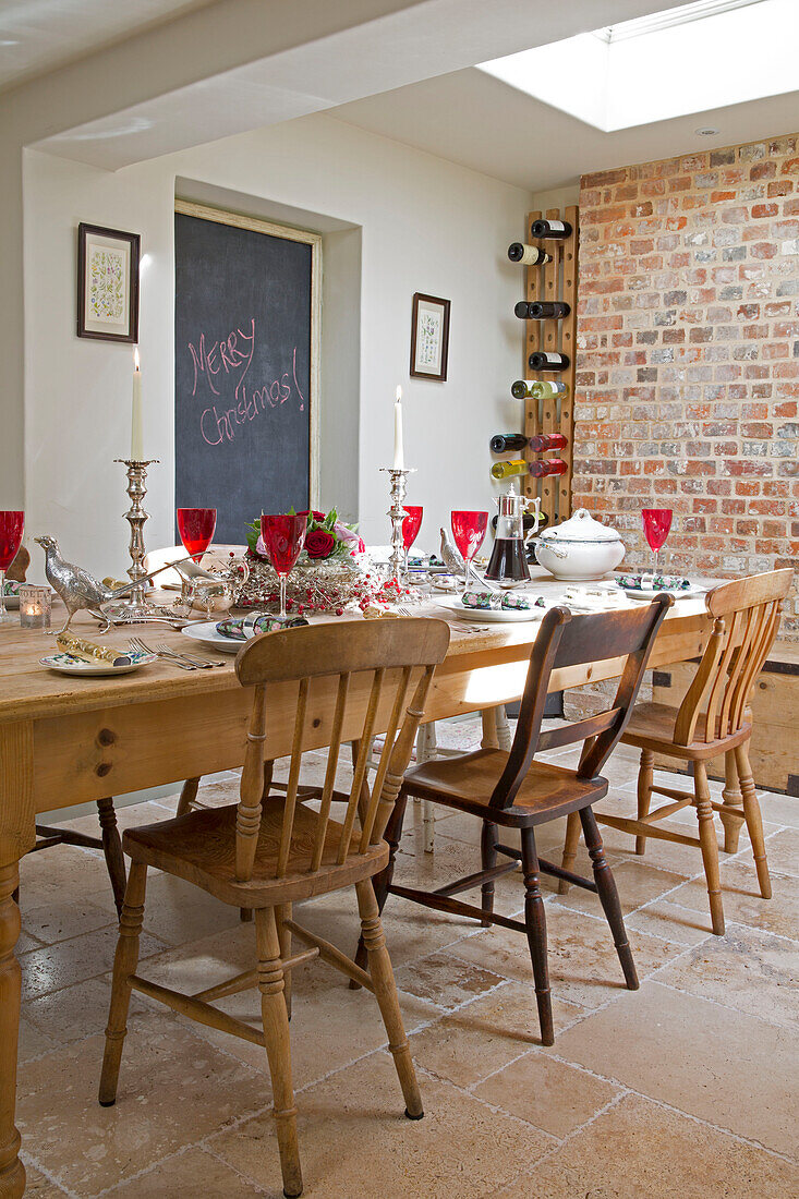Rote Gläser auf hölzernem Esstisch mit freiliegender Ziegelwand und Kreidetafel im Haus in Berkshire, England, UK
