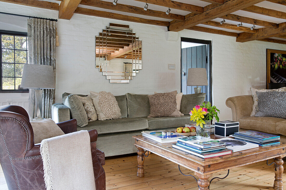 Couchtisch aus Holz mit Wildledersofa und Spiegel im Wohnzimmer mit Holzbalken in einem Cottage in Sussex, England, Vereinigtes Königreich