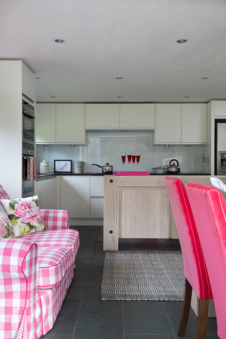 Pink gingham sofa in open plan kitchen with pale wood island unit in Sussex cottage   England   UK