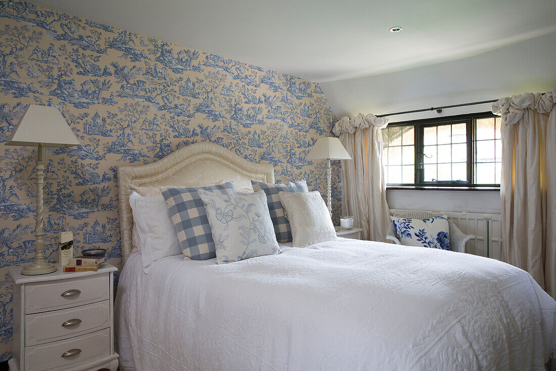 Gemusterte Tapete mit zwei Lampen am Bett im Schlafzimmer in einem Cottage in Sussex, England UK
