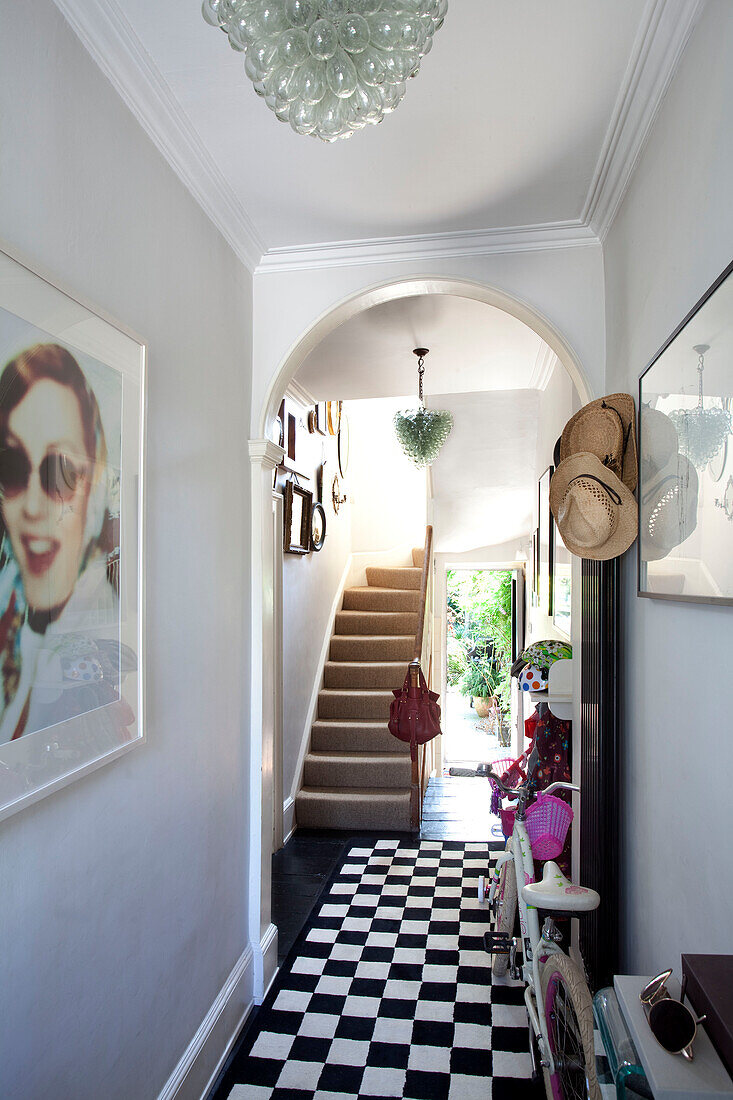 Framed artwork and sunhats with checked rug in hallway of London townhouse, England, UK