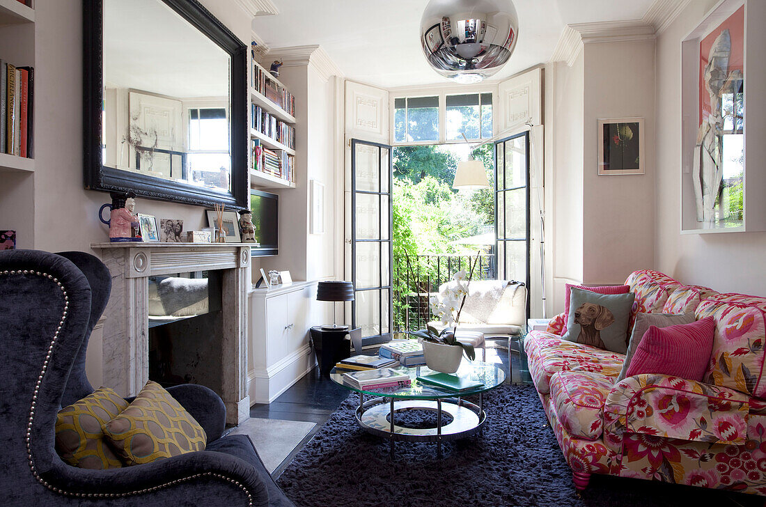 Pink floral sofa and glass topped table with open French windows in living room of London townhouse, England, UK