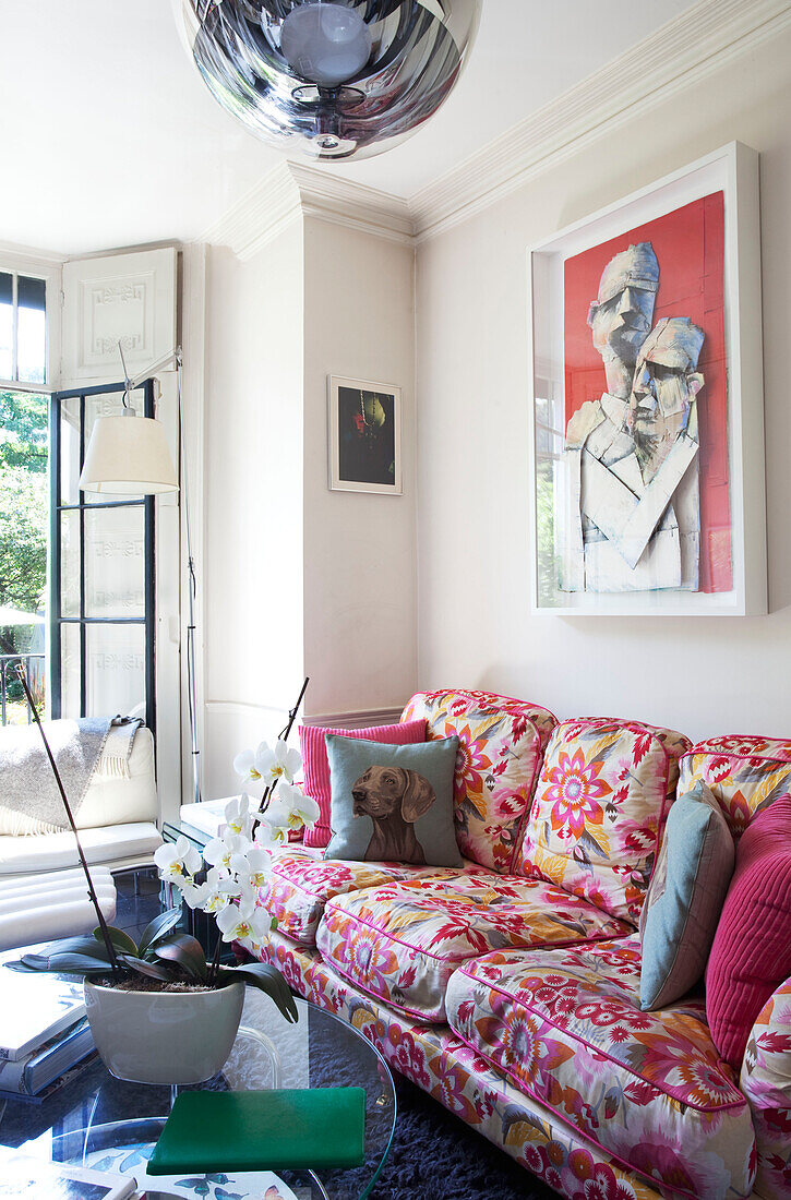 Kunstwerk über einem rosa geblümten Sofa mit Orchidee im Wohnzimmer eines Londoner Stadthauses, England, UK