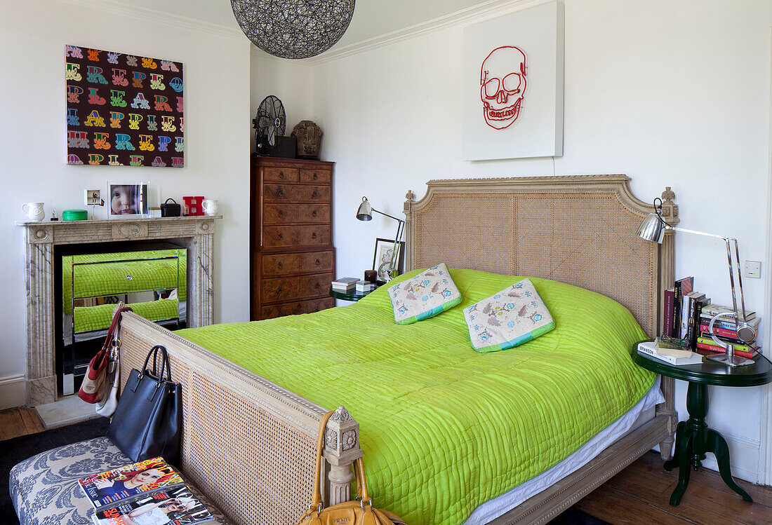 Lindgrüne Bettdecke mit Holztruhe und bunten Kunstwerken im Schlafzimmer eines Londoner Stadthauses, England, UK