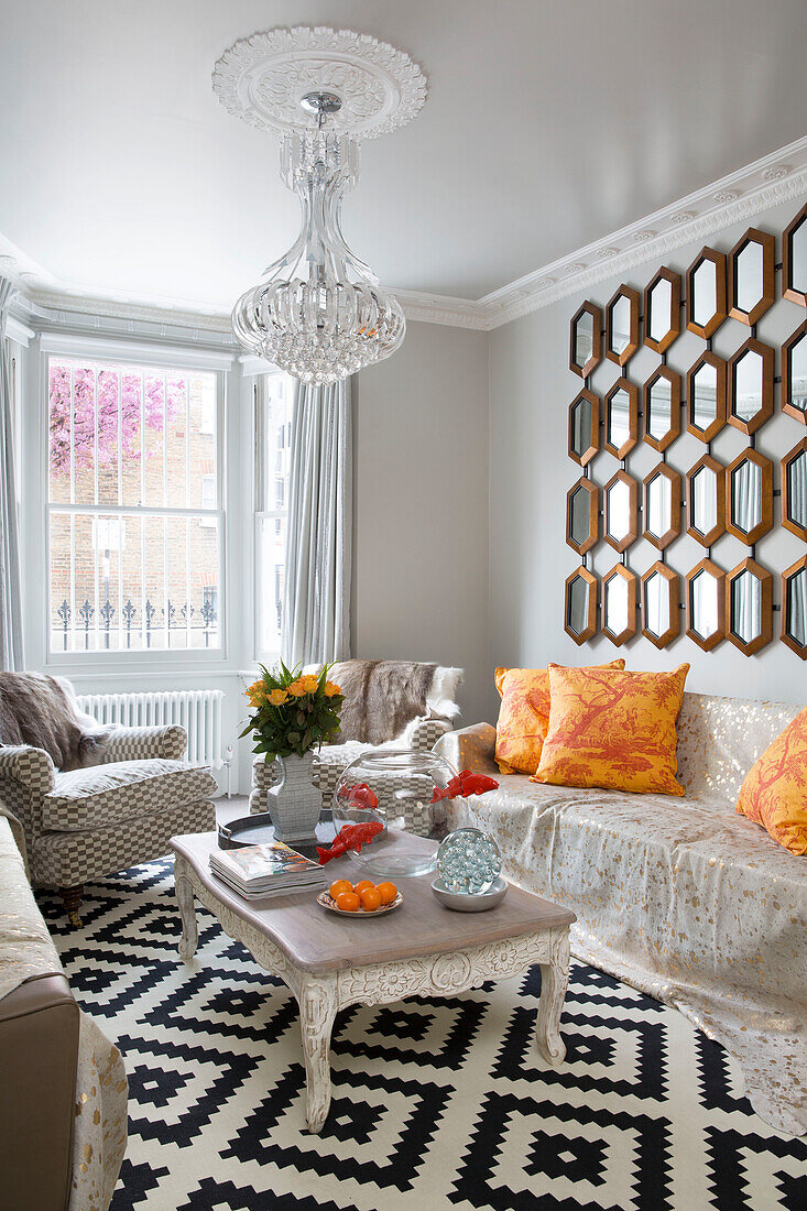 Spiegel über dem Sofa mit gelben Kissen und geometrisch gefliestem Boden im Wohnzimmer eines Hauses in London, England, UK