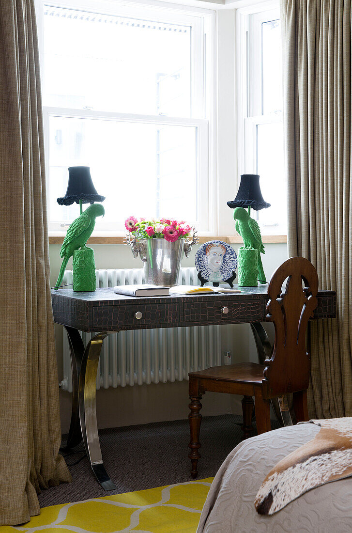 Ein Paar grüne Papageienlampen auf einem Schreibtisch mit Stuhl am Fenster in einem Londoner Haus, England, UK