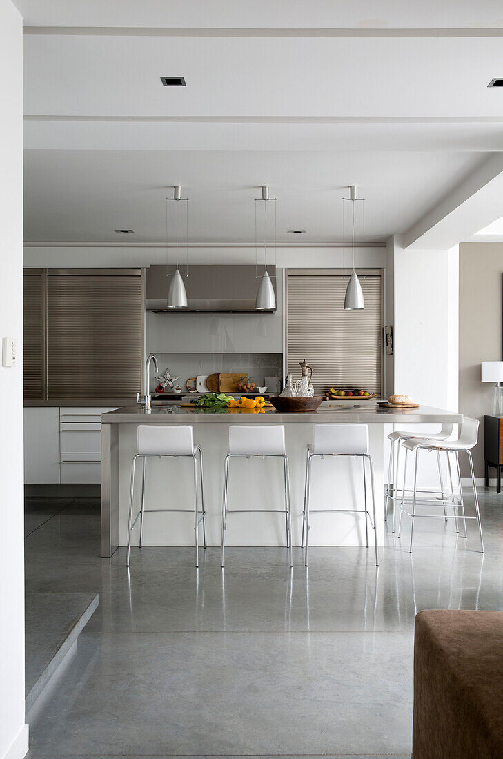 Bar stools at kitchen island with metallic pendant lights in contemporary Sussex home, England, UK