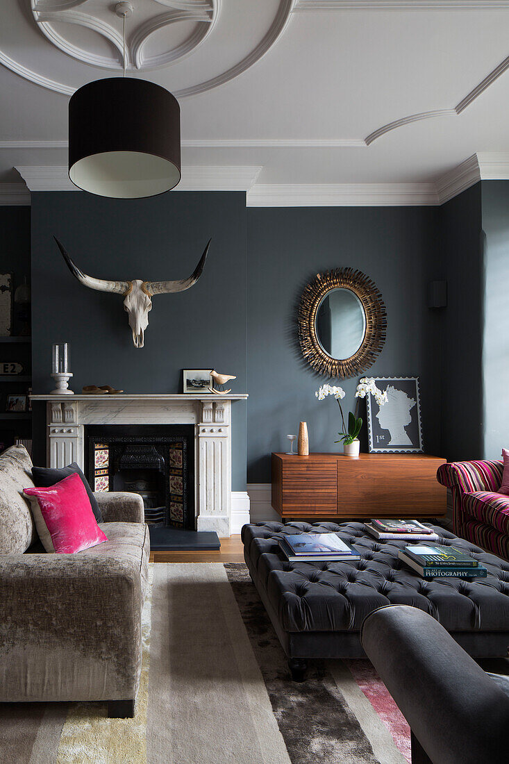 Geknöpfter Ottoman und Sofa mit Vintage-Spiegel und Geweih im Wohnzimmer in Sussex, England, UK