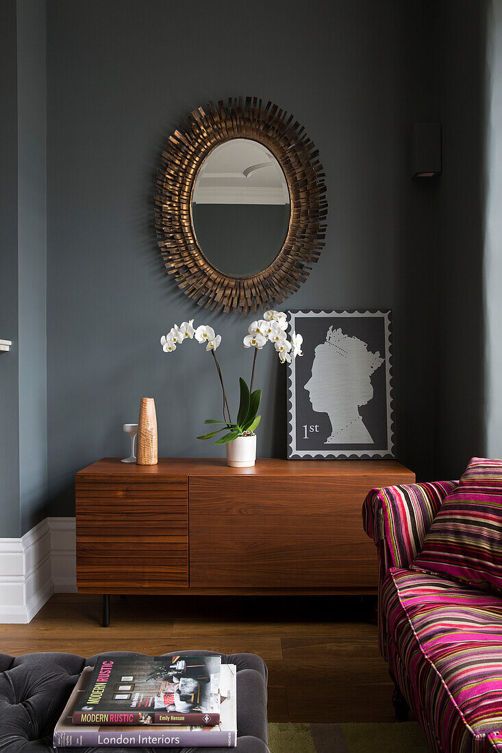 Vintage mirror above wooden sideboard with orchid and large postage stamp in contemporary Sussex home, England, UK