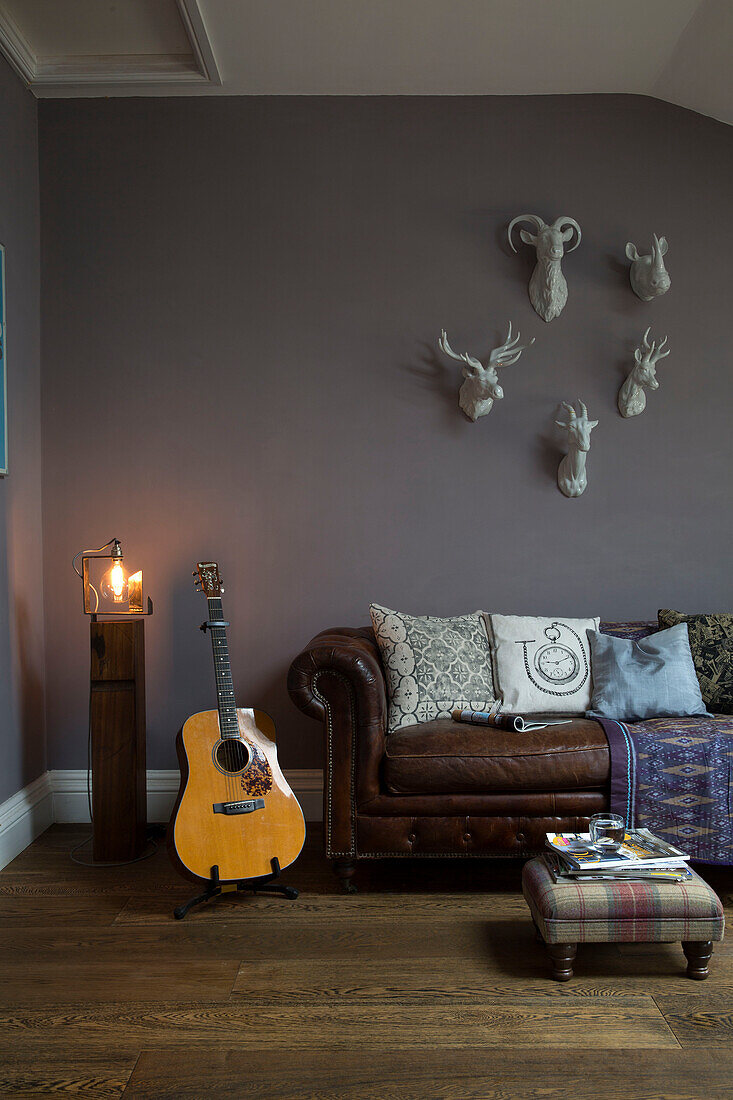 Gitarre mit braunem Chesterfield unter montierten Tierköpfen in einem Haus in Sussex, Großbritannien
