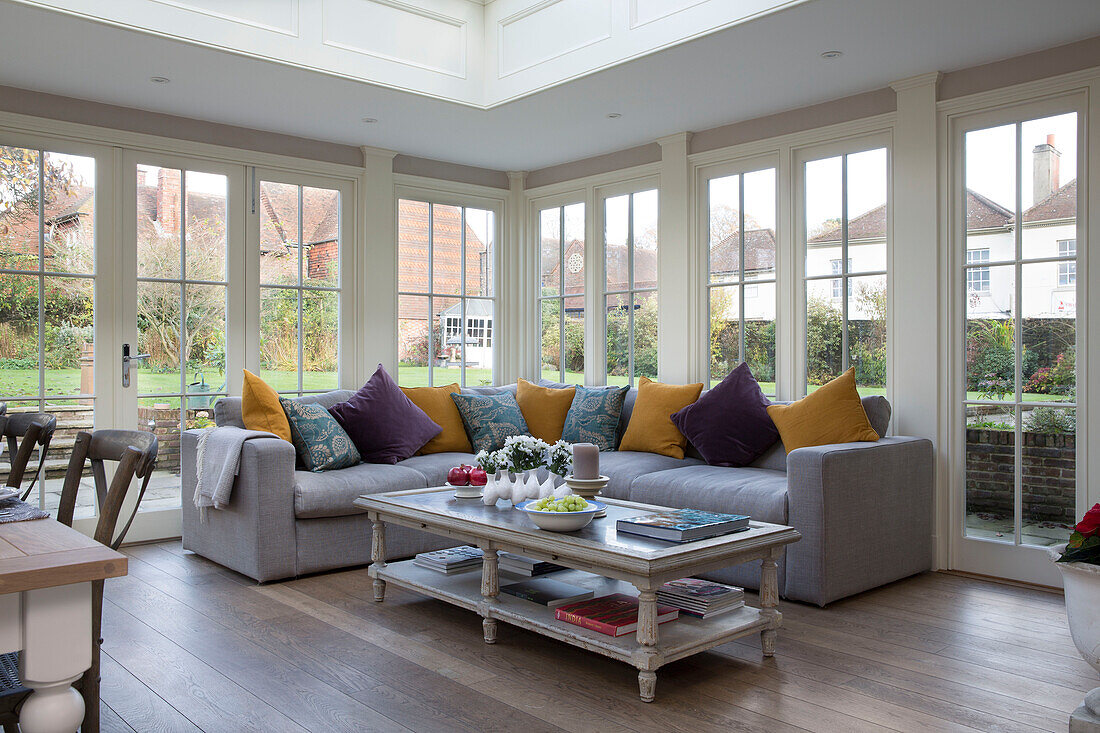 Purple and yellow cushions on sofa with coffee table in conservatory of Surrey home,  England,  UK