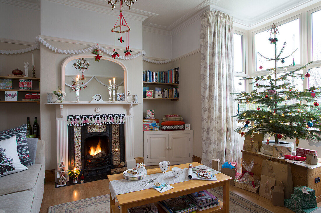 Weihnachtsgeschenke unter Baum mit beleuchtetem Feuer im Wohnzimmer von Dronfield home Derbyshire England UK