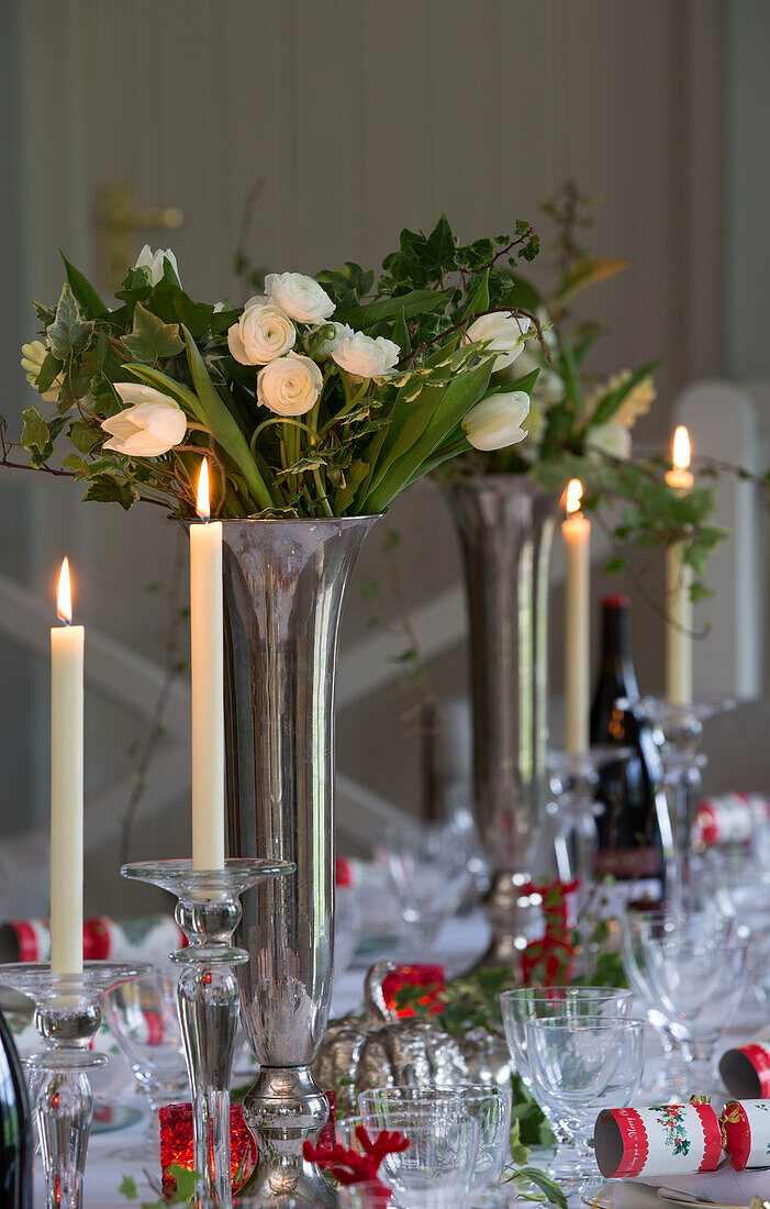 Kerzen und weiße Rosen als Tafelaufsatz auf dem Esstisch zu Weihnachten in einem Haus in Lymington, Hampshire, Großbritannien