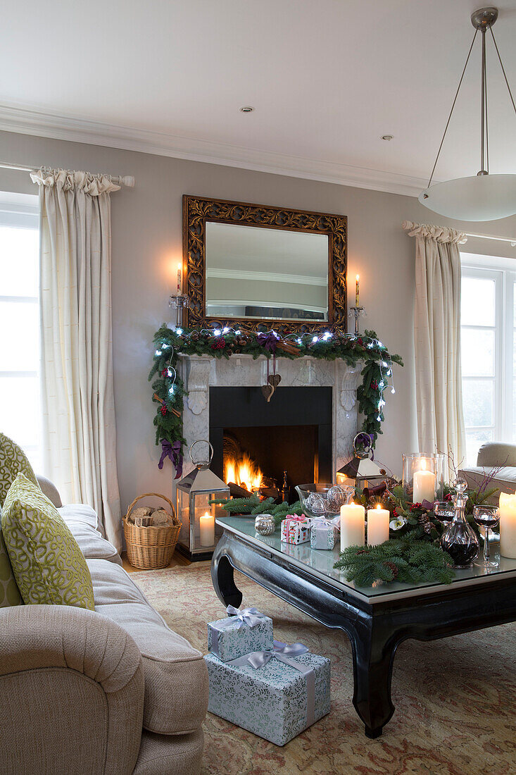 Lichterketten auf Weihnachtsgirlande über beleuchtetem Feuer mit brennenden Kerzen im Wohnzimmer eines Hauses in Chobham Surrey England UK