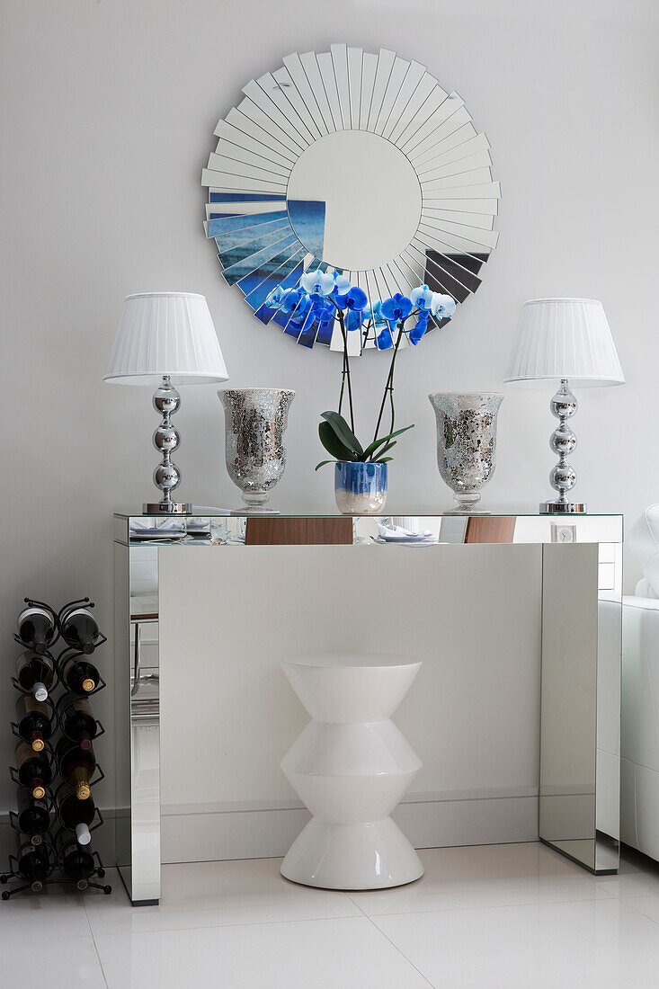Ein Paar passende Lampen mit rundem Spiegel und Weinregal auf einer Spiegelkonsole in einem modernen Londoner Haus UK
