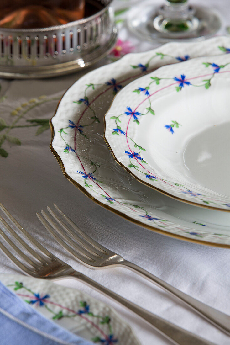Floral gemusterte Teller mit silbernen Gabeln auf bestickter Tischdecke in einem britischen Bauernhaus